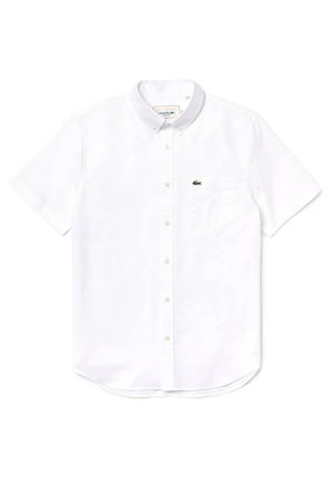 Chemise blanche à manches courtes en coton, avec une poche sur le côté gauche de la poitrine ornée d'un logo Lacoste vert, ourlet arrondi.