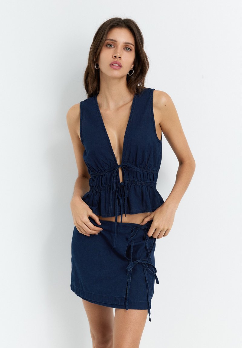 Mørkeblå to-delt sæt med en peplum-top med dyb V-udskæring og justerbare bånd, parret med en mini-nederdel med sidebånd.