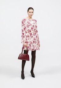 Φλοράλ φόρεμα με μακριά μανίκια και βολάν στο τελείωμα, με ροζ και μπορντό λουλούδια σε ανοιχτό φόντο. Συνδυασμένο με μπορντό τσάντα χειρός και μαύρες γόβες.