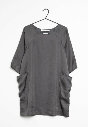 Grå løstsiddende kjole med trekvartlange ærmer og store sidelommer, hængende på sort bøjle mod hvid baggrund.