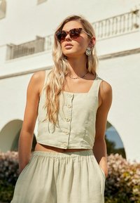 Világoszöld len crop top gombokkal és négyzet alakú neckline-nel, világoszöld elasztikus derekú sorttal párosítva; jellemzője a laza illeszkedés és a sima textúra.
