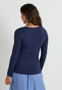 Top de manga larga azul marino con cuello redondo, textura suave, diseño ajustado, combinado con una falda a rayas azul y blanca.