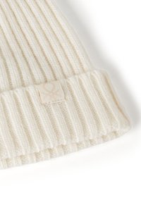 Berretto a maglia crema con texture a costine e un'etichetta in tessuto cucita con un logo sottile. Il materiale è morbido e caldo.