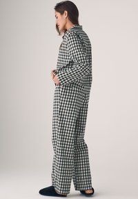 Fekete-fehér kockás pizsama szett, laza szabású nadrággal és gombos, galléros felsővel. Puha anyagból készült, hosszú ujjal.