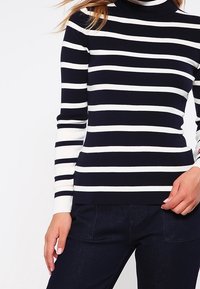 Laivastonsininen ja valkoraidallinen pooloneule pitkähihaisilla hihoilla, resuinen pinta, vartalonmyötäinen malli ja yhtenäinen laivastonsininen helma vyötäröllä.