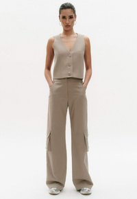 Beige cropped vest met drie knopen en wijde cargobroek met zijzakken. Glad textuur en een ontspannen fit. Zilveren sneakers.