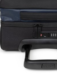 Zwarte geribbelde trolleykoffer met een blauw bovenste gedeelte, dubbele ritssluitingen, combinatiehangslot en een uitschuifbare handgreep voor eenvoudig manoeuvreren.