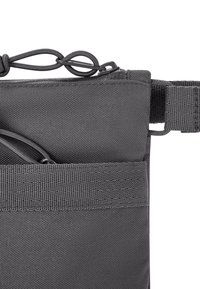 Borsa in tessuto grigia con superficie testurizzata, dotata di chiusura superiore con coulisse e attacco laterale per la tracolla. Due tasche anteriori per la conservazione.