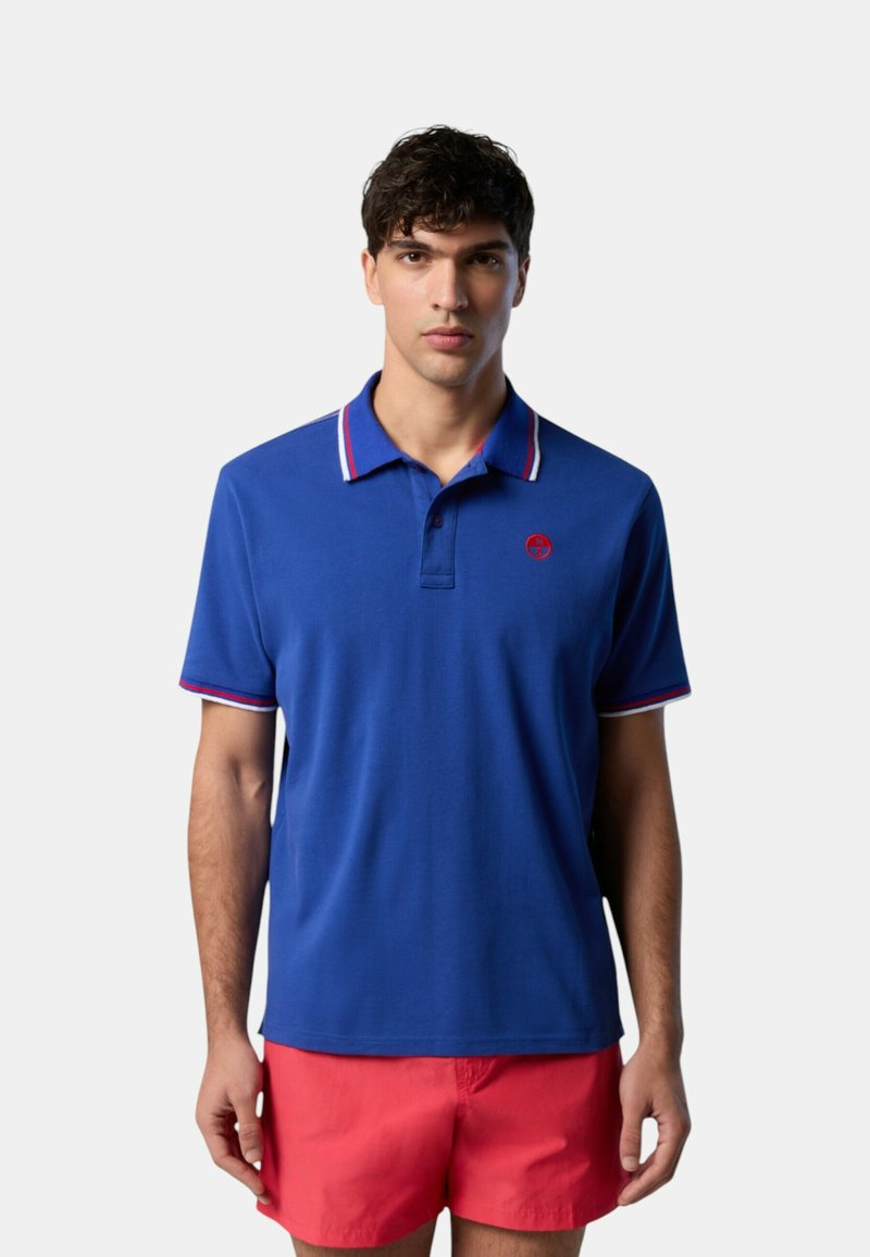 Polo blu con colletto striato rosso e bianco, con un piccolo logo sul petto, realizzato in tessuto liscio, maniche corte.