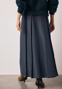 Pikk mereväesinine plisseeritud seelik, sileda tekstuuriga, kombineeritud robustse kootud kampsuniga. Komplekt on minimalistliku ja elegantse disainiga.