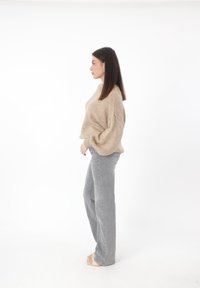 Suéter beige de gran tamaño con hombros caídos, combinado con jeans de tiro alto en gris claro. Modelo de pie de lado sobre un fondo blanco.
