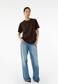 Brun bomulds t-shirt med korte ærmer, parret med lyseblå brede bukser. Sættet har en afslappet pasform og en glat tekstur.