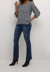 Bluse med blomsterprint i blå med V-hals og trekvartærmer, parret med blå flagrende jeans og sorte hælede ankelstøvler.
