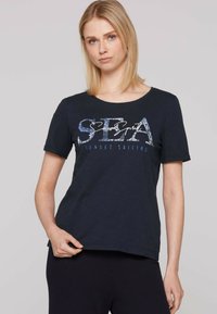 Camiseta de algodón azul marino con mangas cortas, presenta un estampado gráfico "SEA Sunset Sailing" en azul y blanco en la parte frontal.