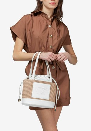 Bolso redondo de fibras naturales trenzadas con acentos de cuero blanco y parche con logotipo. Cierre de cordón en la parte superior, asas cortas y textura de fibra natural.