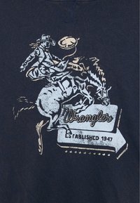 T-shirt in tessuto blu navy con una grafica di un cowboy su un cavallo che scalpita, accompagnato dalla scritta "Wrangler Established 1947" in bianco e oro.