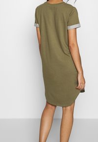 Oliwkowa sukienka koszula z krótkimi rękawami i podwiniętymi mankietami w jasnoszarym kolorze. Miękka tkanina, lekko zaokrąglony dół, swobodny krój.