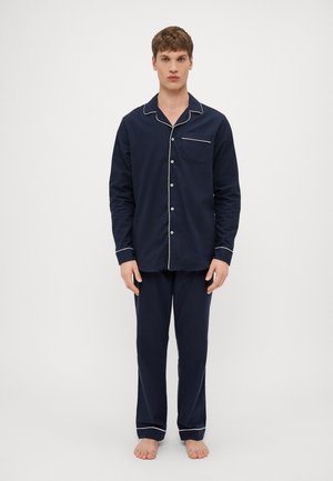 Navy blue cotton pajama set with white piping, featuring a button-up shirt with a pocket and matching pants with cuffed hems.