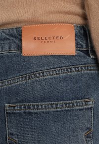 Jeans i denimtyg med en ljusblå tvätt. Har en beige läderetikett med "SELECTED FEMME" präglad. Synlig sömnad och detaljering av fickor.