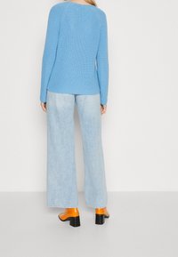 Maglione lavorato a maglia azzurro chiaro con maniche lunghe, abbinato a jeans a gamba larga azzurro chiaro e mule con tacco arancio. Vista posteriore dell'outfit.