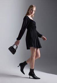 Robe noire à manches longues, taille froncée et jupe évasée. Assortie à un petit sac noir à pois argentés et des bottines pointues.