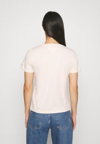 Camiseta corta de manga corta rosa claro con un corte relajado, que presenta un escote en V y una textura de algodón suave, combinada con unos jeans de mezclilla azules.