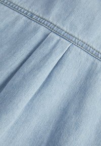 Tessuto in denim azzurro chiaro con texture visibile e un leggero lavaggio. Presenta pieghe lungo la cucitura e dettagli di cucitura a contrasto.