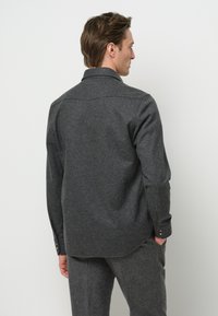 Camicia in lana grigia scura con colletto, maniche lunghe e polsini abbottonati. Presenta un'orlo arrotondato e una trama semplice, adatta per essere indossata a strati.