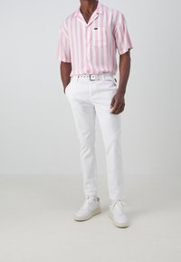 Kortärmad rosa randig skjorta med bröstficka, kombinerad med vita slim fit-byxor och vita sneakers med texturerade sulor.