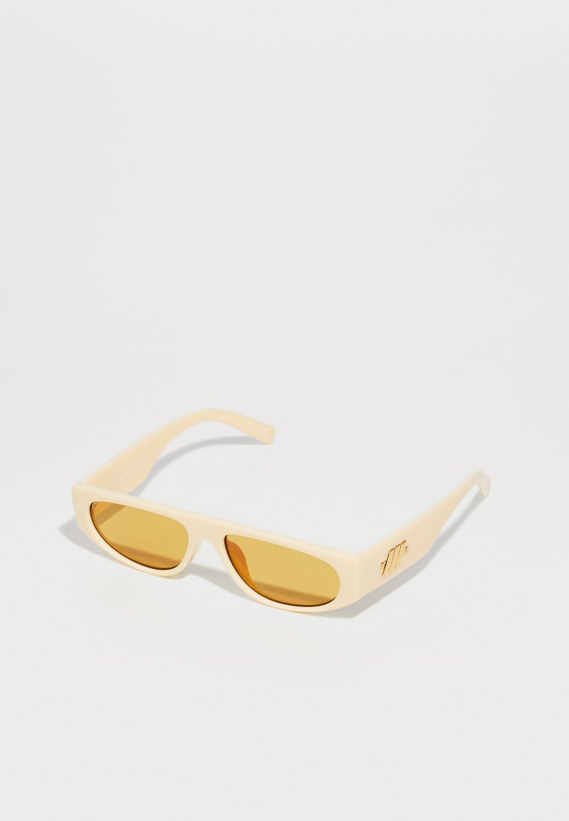 Occhiali da sole beige con montatura rettangolare, lenti color giallo e una superficie liscia e opaca. Presentano un dettaglio del logo dorato sul lato.