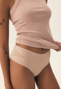 Beżowa bezszwowa bielizna z wysokim stanem, z siateczkowymi detalami. Tkanina jest gładka, elastyczna i dopasowująca się do ciała.