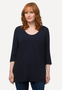 Navyblaues Oberteil mit drei Viertelärmeln aus weichem Stoff, weitem Rundhalsausschnitt und lockerer Passform, kombiniert mit Jeans.