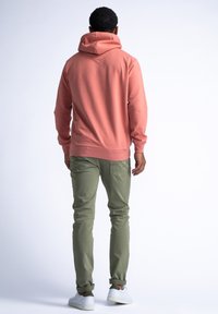 Sudadera rosa con un bolsillo canguro y capucha ajustable, combinada con pantalones cargo verde oliva. El modelo lleva zapatillas blancas.