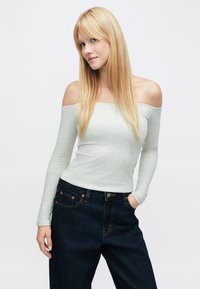 Gaiši pelēka, no pleciem kaila ar garām piedurknēm topiņš no mīksta materiāla, kombinēts ar tumši ziliem džinsa biksēm ar oranžām šuvju akcents detaļām.