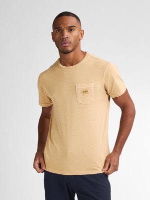 Beige kortærmet T-shirt lavet af blødt stof, med en brystlomme og et lille mærke. Rund halsudskæring og afslappet pasform.