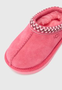 Rosa Wildleder-Hausschuh mit einem weichen, flauschigen Innenfutter. Mit dekorativen Nähten entlang des Kragens und einer Gummisohle. UGG-Logo angebracht.