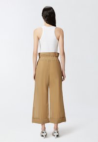 Smeđe široke hlače izrađene od teksturiranog, laganog materijala, sa elastičnom trakom u struku i skraćenim rubom. Uparene s metalik petama.