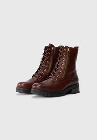 Botas de tobillo de cuero marrón con cordones en la parte delantera, cremalleras en los laterales y una suela de goma robusta con un agarre texturizado. Detalles en dorado.