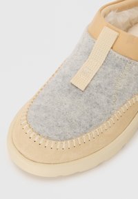 Grå ulloverdel med beige semsket skinn detaljer, lukket tå, flat gummisåle, og en vevd tekstilløkke for enkel påkledning. Håndsydd detaljering.