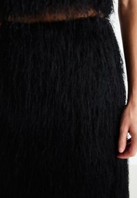 Black, textured fashion item featuring a fuzzy, shaggy material. Shaped with a fitted waist and flowing lower portion.