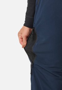 Eine Hand, die eine dunkelb blaue Kleidungstasche mit schwarzer Mesh-Belüftung und Reißverschluss-Hebeln öffnet, wobei das atmungsaktive Mesh-Futter innen sichtbar ist.