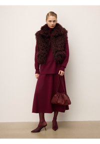 Tenue bordeaux mettant en avant un gilet texturé et duveteux porté sur une robe en maille ajustée. Les accessoires comprennent un sac à main plissé et des talons pointus.