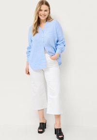 Chemise boutonnée en lin bleu clair avec un col en V, des manches longues et une coupe décontractée, associée à un pantalon large blanc et des mules à talons blocs noirs.