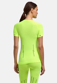 Woman with brown hair in a ponytail wearing a bright yellow-green athletic top and matching leggings with black line patterns, facing away.