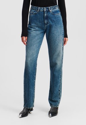 Hochtaillierte blaue Jeans aus Denim mit geradem Bein, ausgestattet mit fünf Taschen und einem Knopfverschluss, präsentiert mit schwarzen spitzen Schuhen.