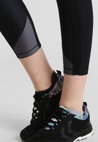 Leggings capri neri con pannelli laterali grigi, caratterizzati da una texture liscia. Abbinati a sneakers nere con colletto e dettagli decorati.