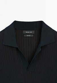 Polo in cotone navy a maglia con un design a coste texture e colletto a V. Presenta un'etichetta del marchio all'interno del colletto.