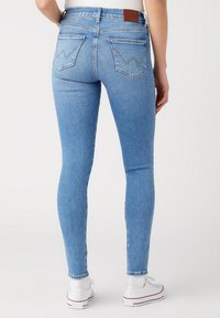 Jeans ajustados de denim azul claro. Presentan dos bolsillos traseros con costuras en forma de zigzag, un parche de cuero marrón en la cintura y un corte estrecho.