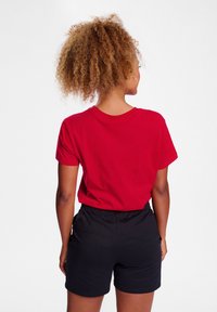 Rød bomulds t-shirt med korte ærmer og rund udskæring, parret med sorte shorts med elastisk talje, set fra bagpå.