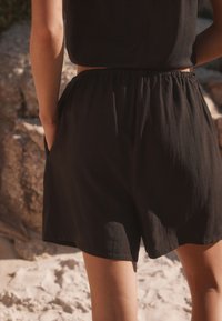 Black shorts made of lightweight fabric with a relaxed fit, featuring an elastic waistband and side pockets, shown from behind.